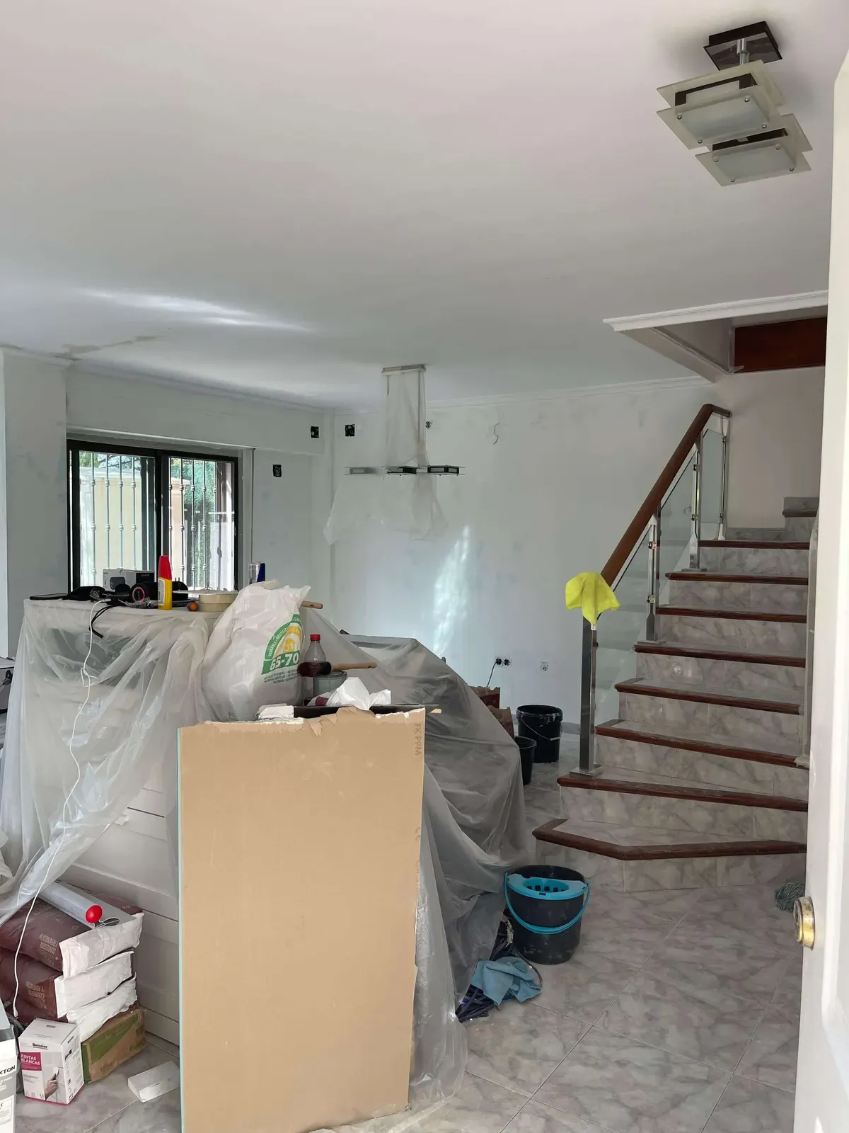 Salón con la escalera al fondo y los muebles protegidos durante la obra